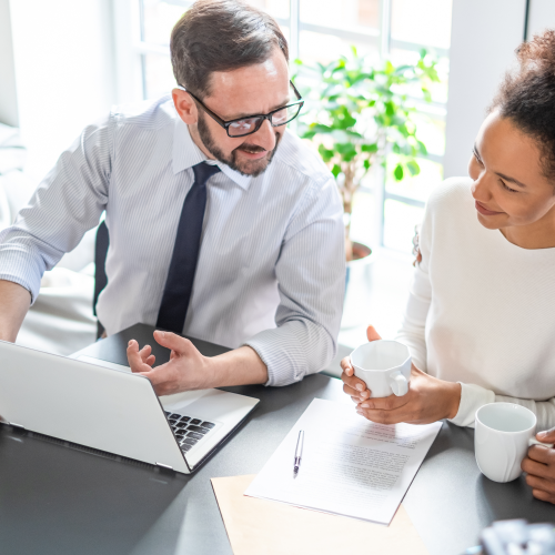 Man pointing at laptop and talking to woman holding a coffee mug